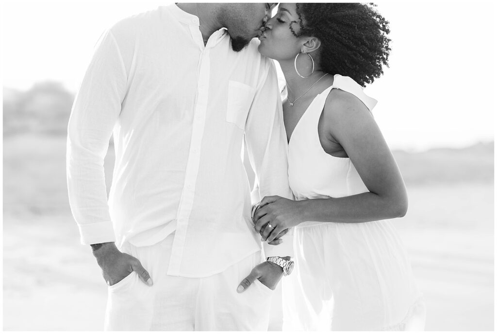 Black and white close-up of the couple sharing a soft kiss, with her hand resting on his chest and engagement ring in view during their beach engagement session.