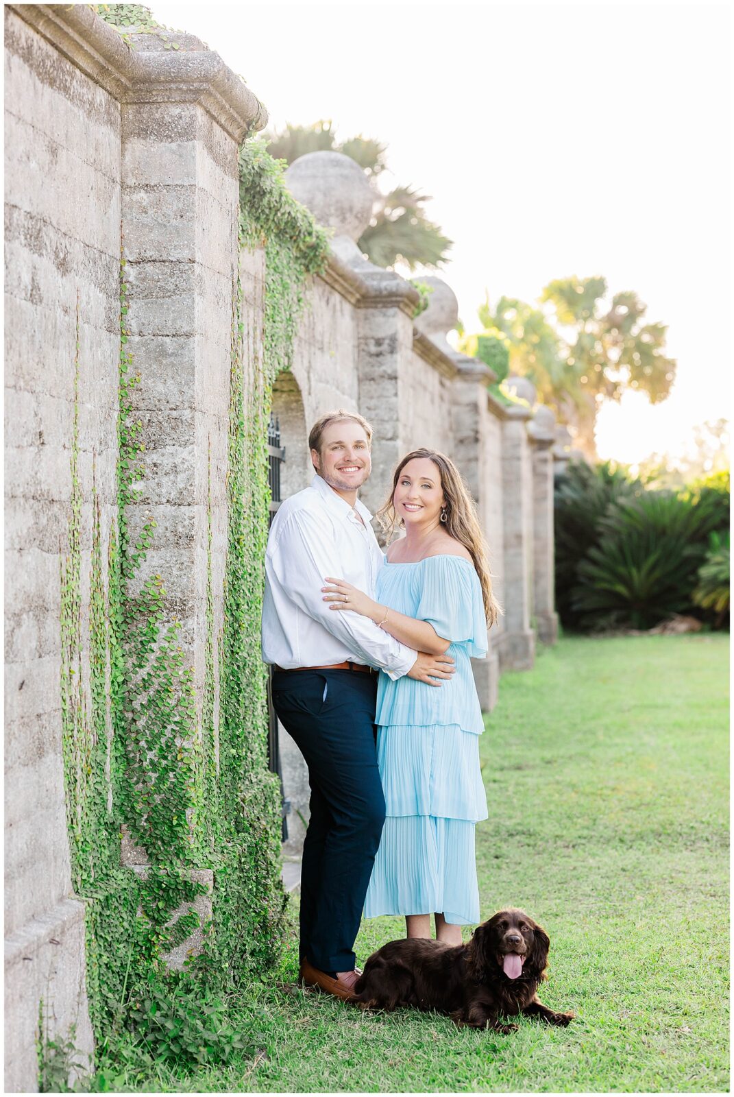 Couple standing together along the historic Dungeness Ruins wall on Cumberland Island while their dog lounges happily in the grass beside them.