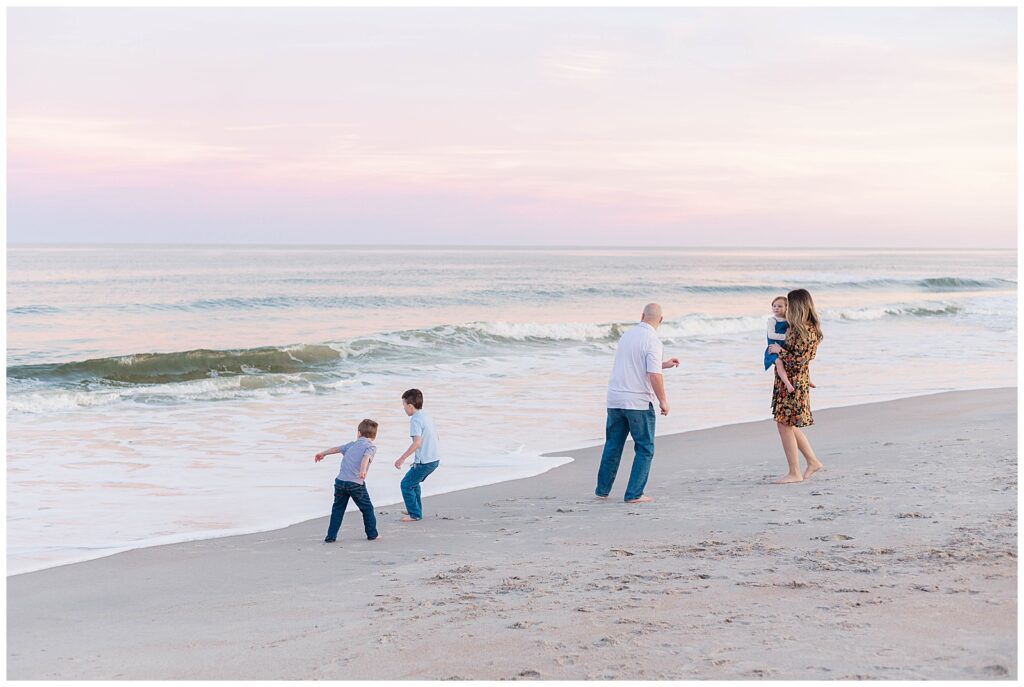Family running along the shoreline at Guana Beach, dad chasing the boys while mom carries daughter during a joyful family session in Ponte Vedra Beach.