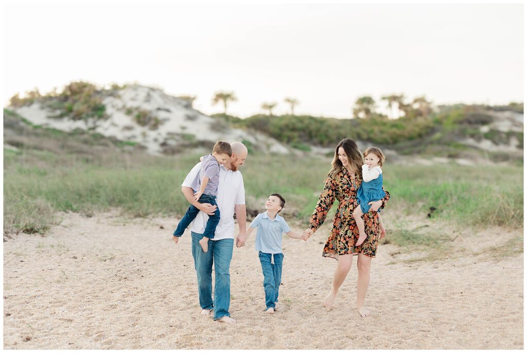Family of five walking barefoot along the sand at Guana Beach, holding hands and smiling during a family session in Ponte Vedra Beach.