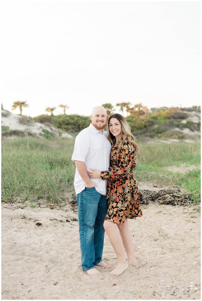 Couple standing close together, smiling at the camera with palm trees and dunes behind them at Guana Preserve in Ponte Vedra.
