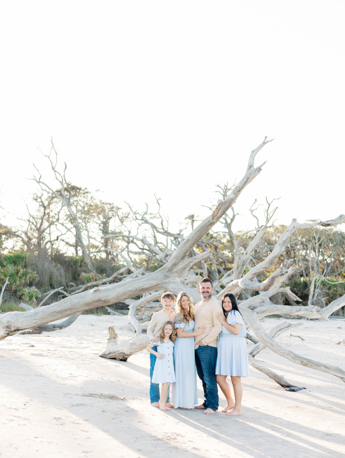 A family of five standing together beneath driftwood trees during a Driftwood Beach family session in Northeast Florida.