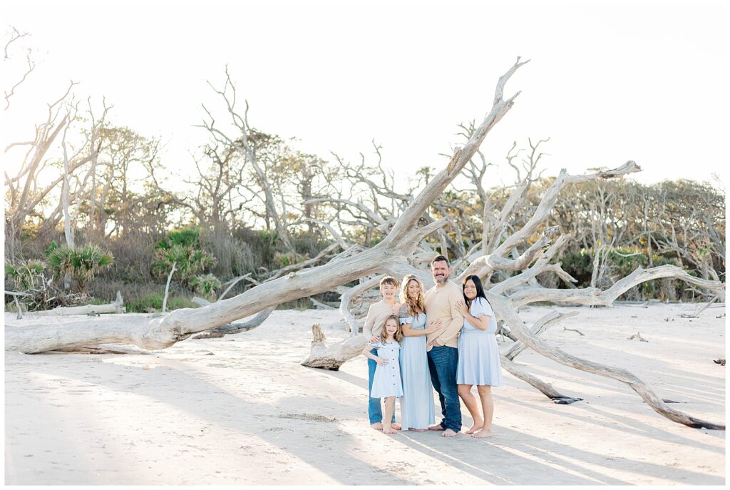 Family standing together among driftwood trees on a quiet Georgia beach at golden hour