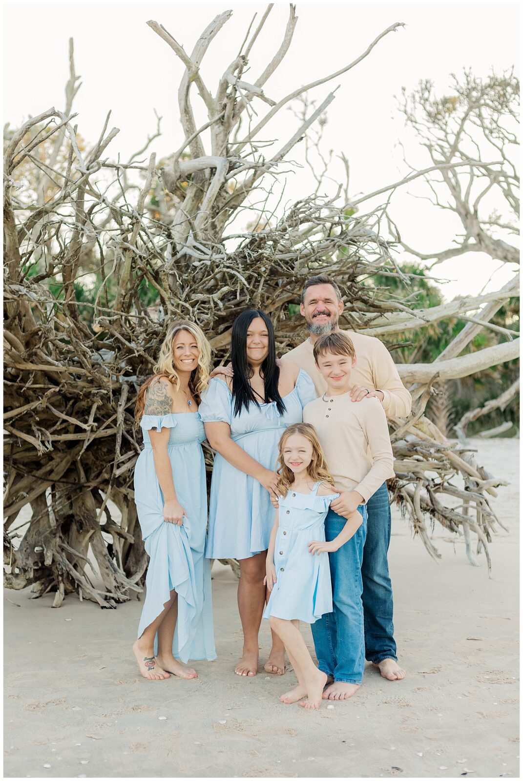 Family standing together among sculptural driftwood with soft coastal light and neutral tones