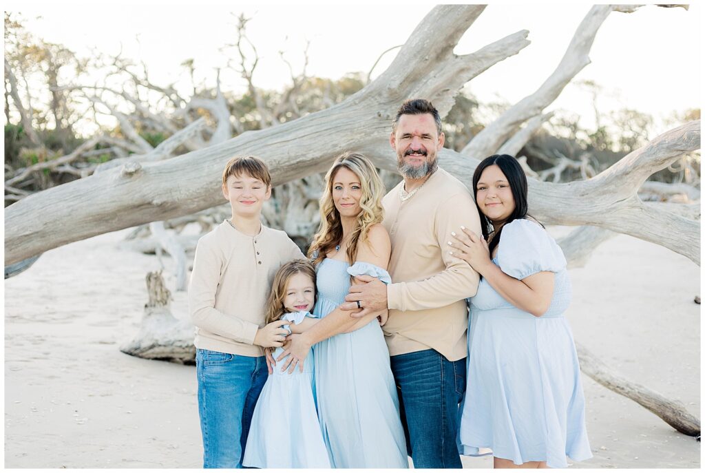 Parents and children posed closely together in front of twisted driftwood branches by the beach