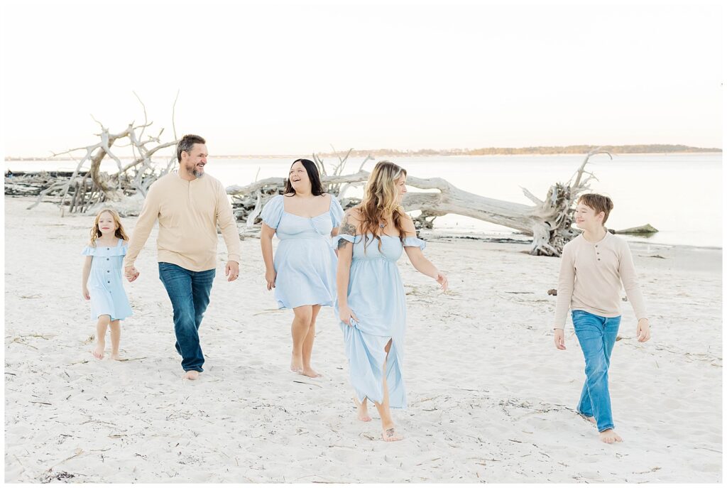Family walking barefoot along the shoreline surrounded by weathered driftwood and open sky