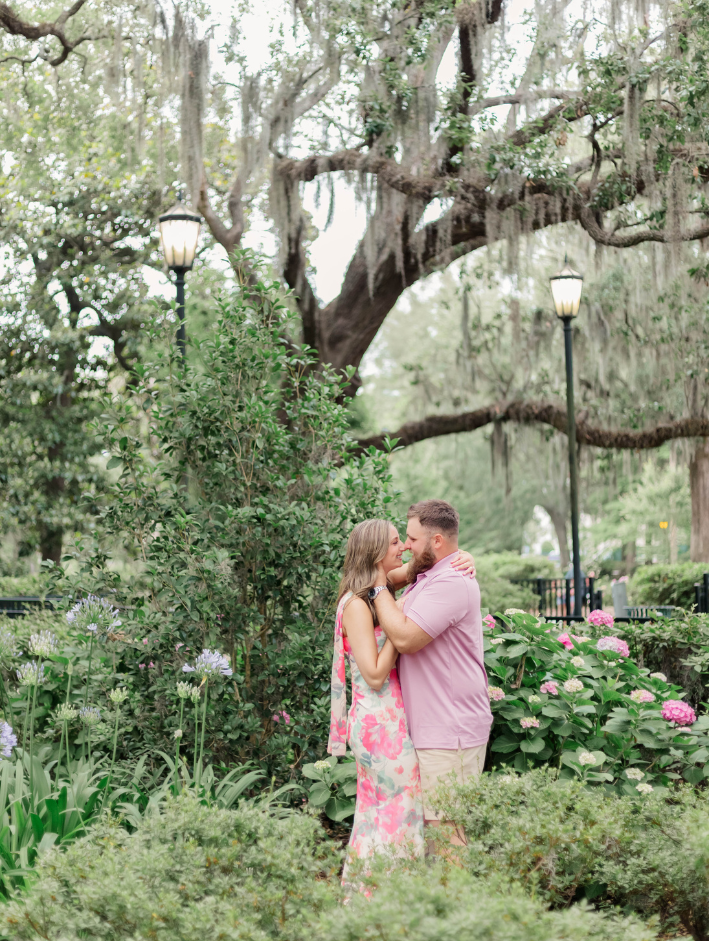 Couple embracing beneath oak trees and blooming hydrangeas during a Forsyth Park engagement session in Savannah