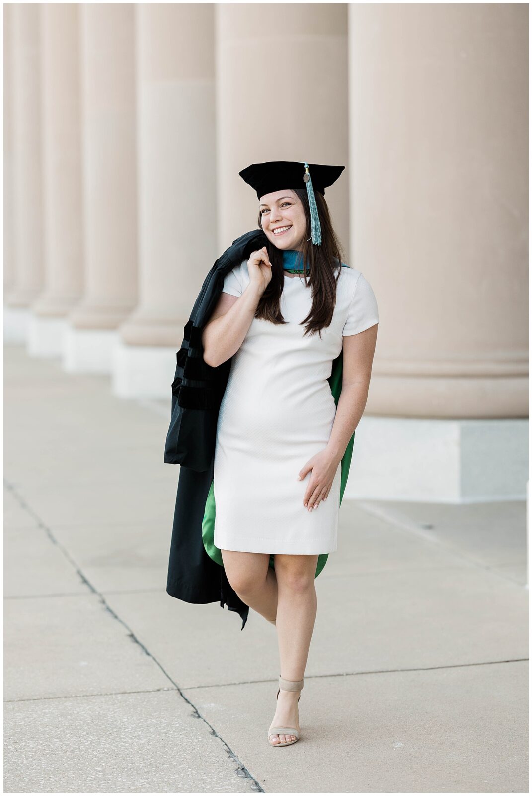 Doctorate graduate from Jacksonville University wearing a white dress and carrying her black graduation gown over one shoulder, smiling proudly in front of neoclassical architecture in downtown Jacksonville.