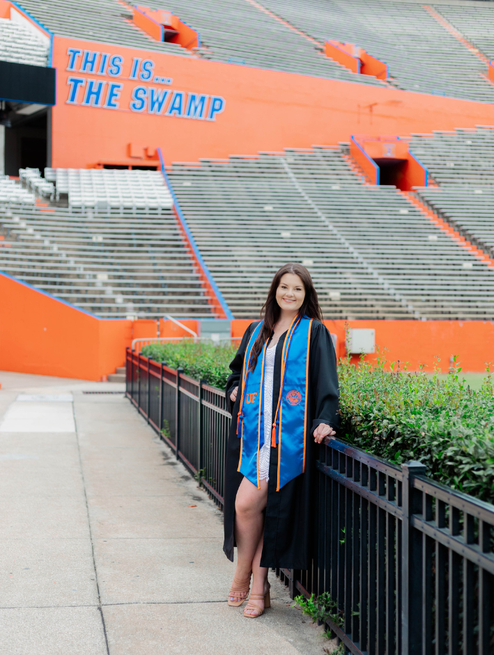 UF grad session at Ben Hill Griffin Stadium featuring a University of Florida graduate in cap, gown, and blue stole