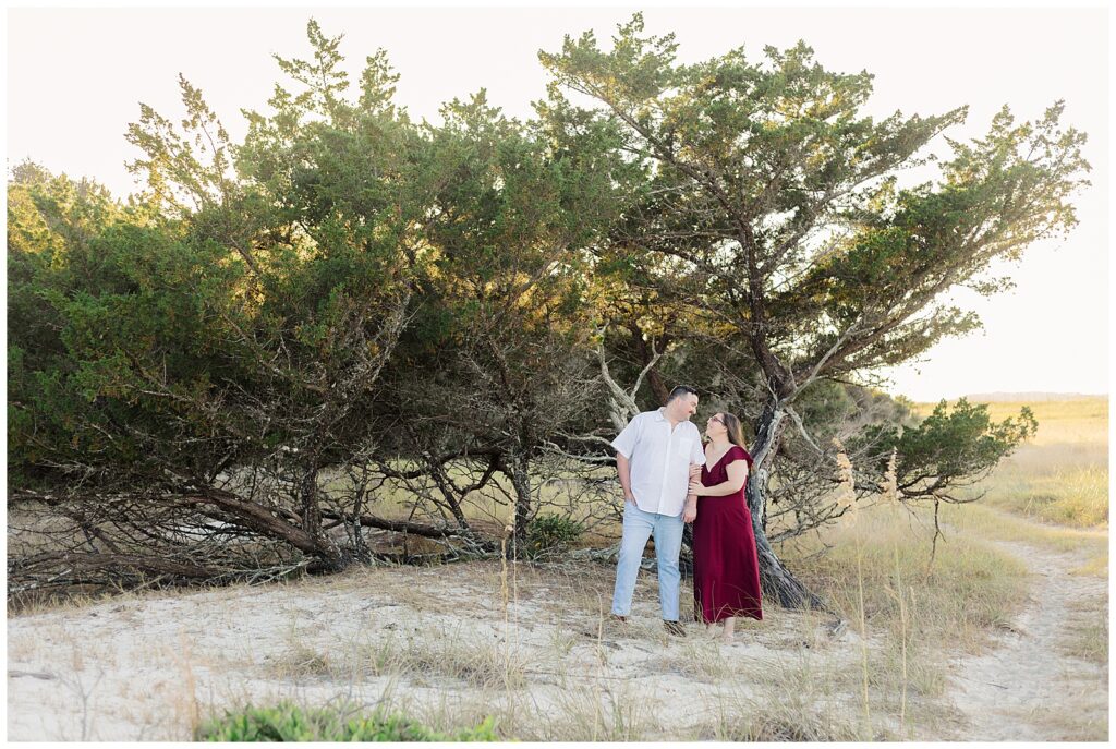 Engaged couple standing together near a curved oak tree with open grassy landscape in the background at Fort Clinch State Park