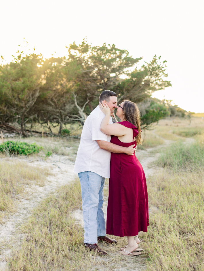 Couple embracing during a Fort Clinch State Park engagement session, standing along a sandy path surrounded by coastal greenery at golden hour.
