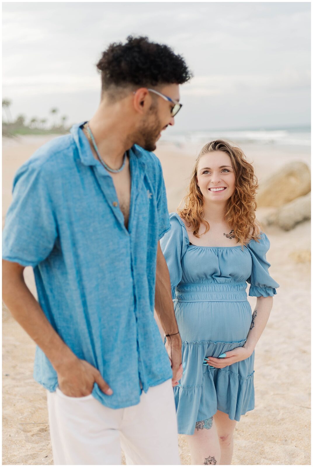 St. Augustine Beach maternity session featuring expecting parents walking hand in hand and sharing quiet moments by the ocean