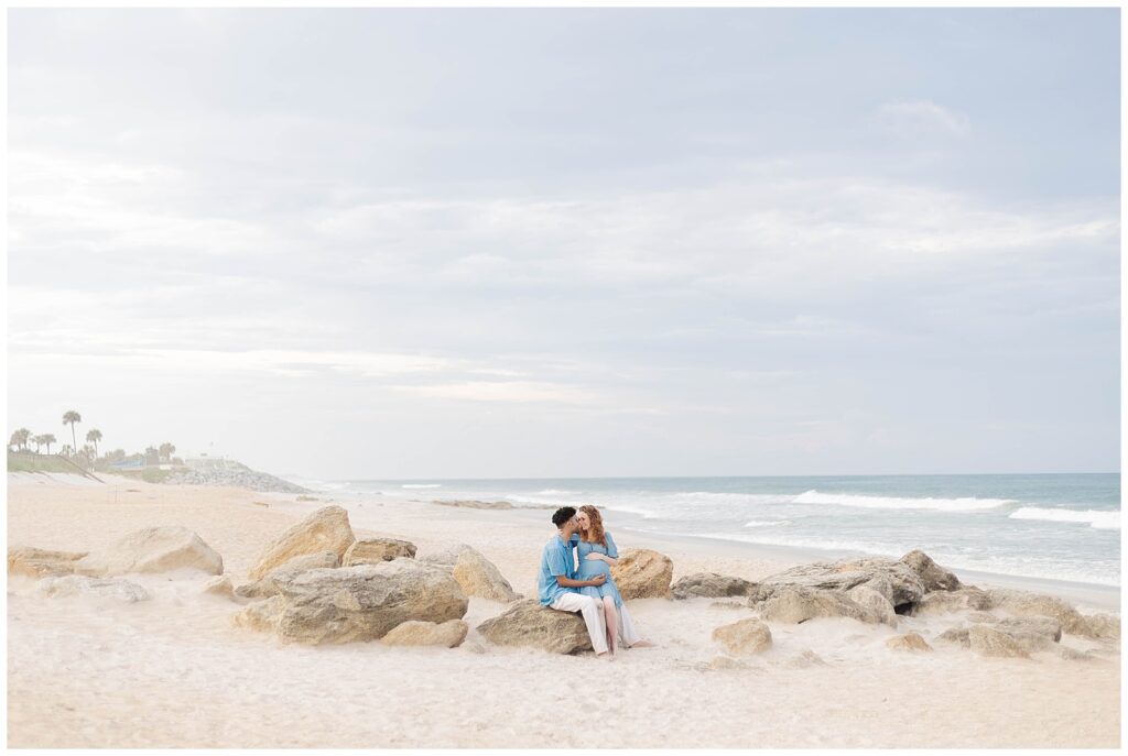 St. Augustine Beach maternity portrait of expecting parents sitting along the shoreline with waves behind them