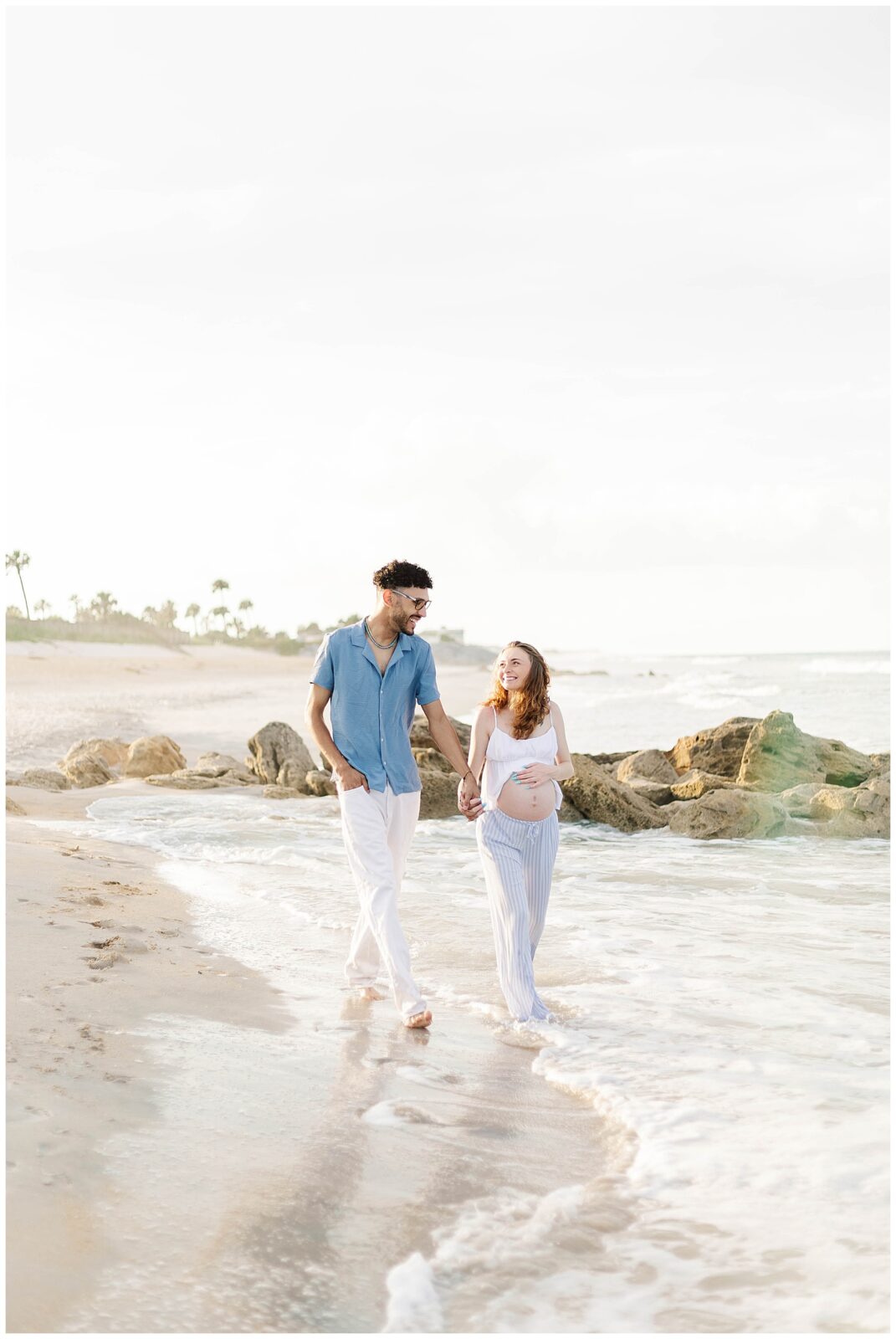 St. Augustine Beach maternity session with expecting parents walking hand in hand along the shoreline at golden hour