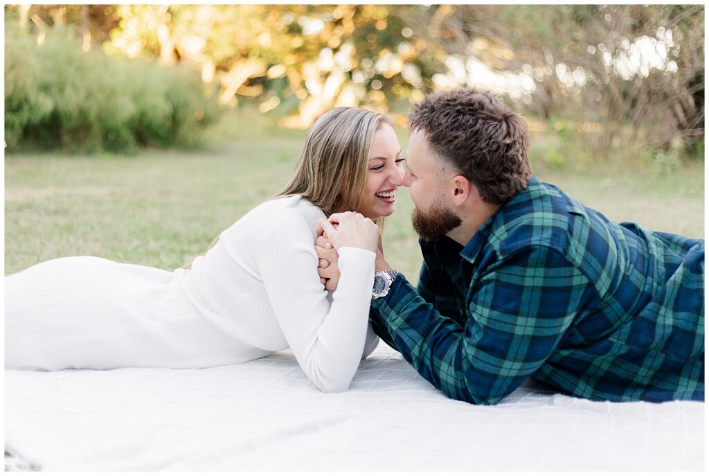 Fort Clinch State Park Engagement Couple lying on a blanket in the grass, laughing nose to nose in warm evening light.